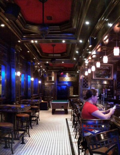 Interior of a dimly lit bar with patrons seated and ornate wooden finishes.