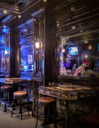 Dimly lit bar with reflective surfaces and stools near a counter.