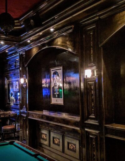 Dimly lit upscale bar with dark wood paneling, wall art, and a pool table.