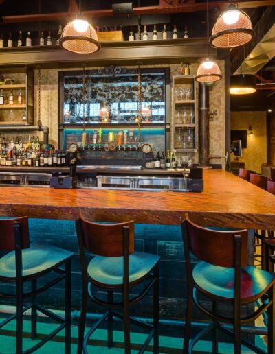 Interior of a modern bar with wooden countertop, bar stools, and a selection of beverages on the shelves.