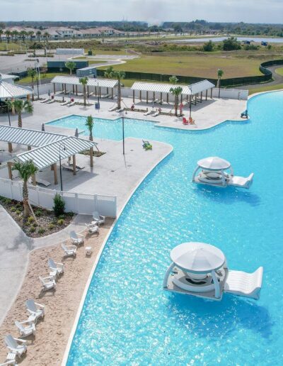 An aerial view of a large, resort-style pool with lounge chairs and cabanas adjacent to residential buildings.