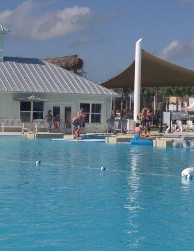 People enjoying a sunny day at an outdoor pool with a white building and sun shades in the background.