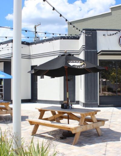 Outdoor seating with picnic benches and umbrellas at a casual dining establishment named fuel.