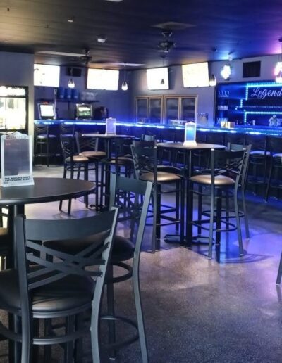 Modern bar interior with blue accent lighting, high stools, and multiple television screens.