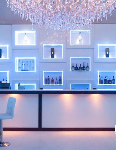 An illuminated modern bar with backlit shelves and a large chandelier.