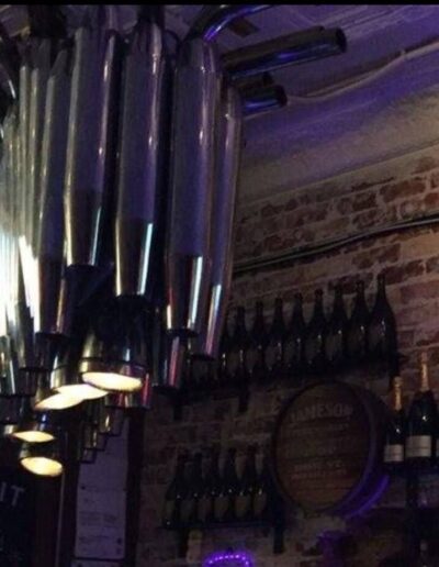 Interior of a dimly lit bar featuring a row of draft beer taps, branded merchandise on the wall, and a selection of bottles on display.