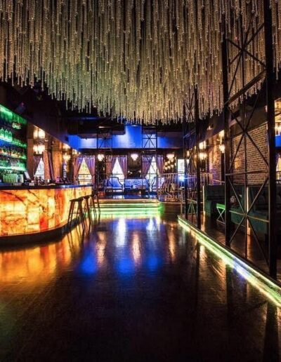 Dimly lit modern bar interior with illuminated counter and hanging crystal decor.