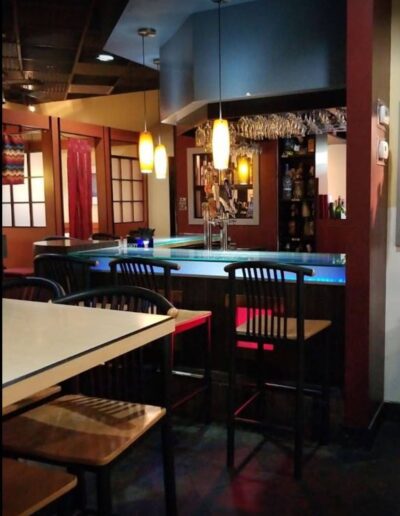 Dimly lit restaurant interior with empty tables and a bar counter in the background.