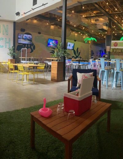 A vibrant beach-themed indoor lounge area with neon signage, casual seating, and a tropical decor vibe.